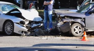 A car accident lawyer standing confidently with arms crossed in front of a car accident scene, wearing a suit and looking directly at the camera.