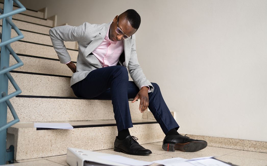 A professional slip and fall attorney sitting at a desk with a laptop, legal documents, and a notepad, looking directly at the camera in an office setting.